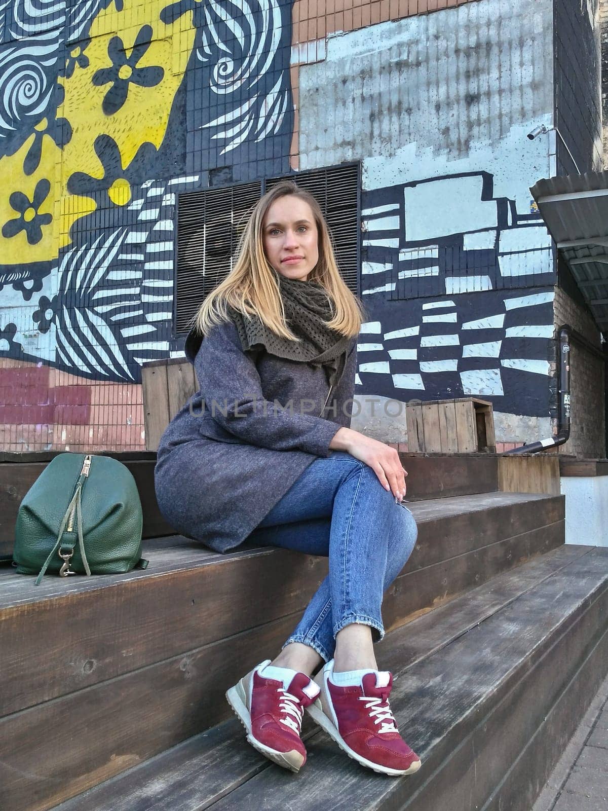 A young woman looks directly into the camera against the backdrop of a painted wall in the fall