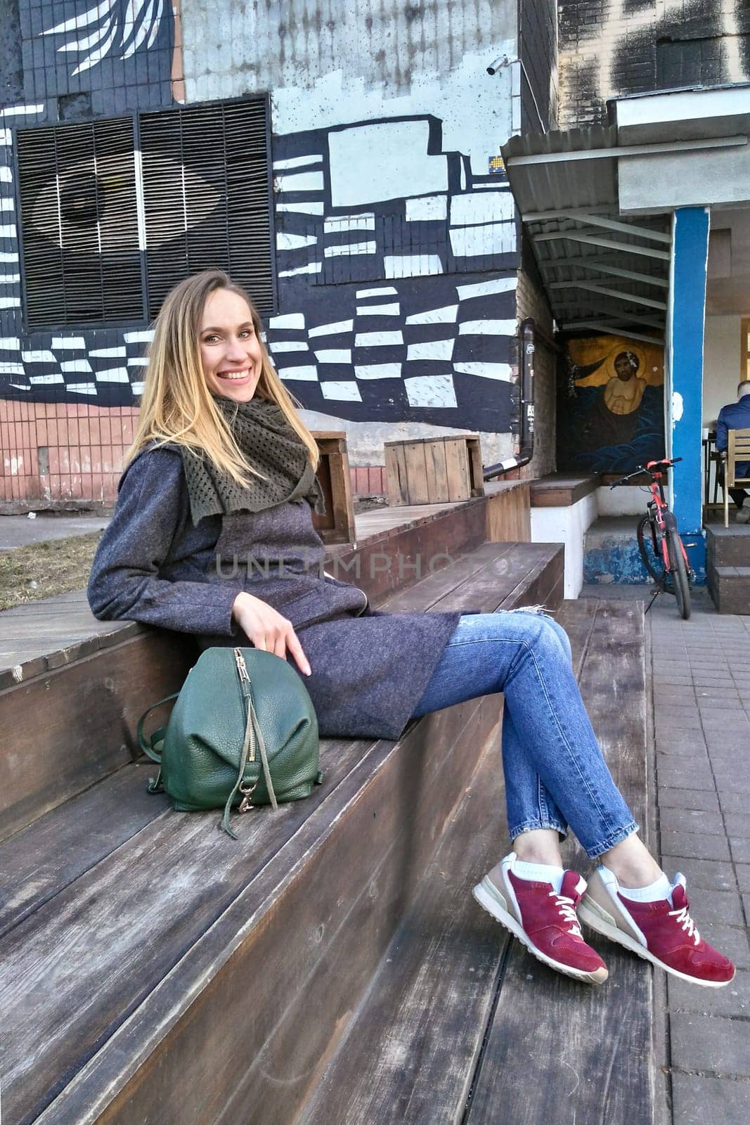 Lucky woman in coat, jeans and sneakers on sits in the old quarter