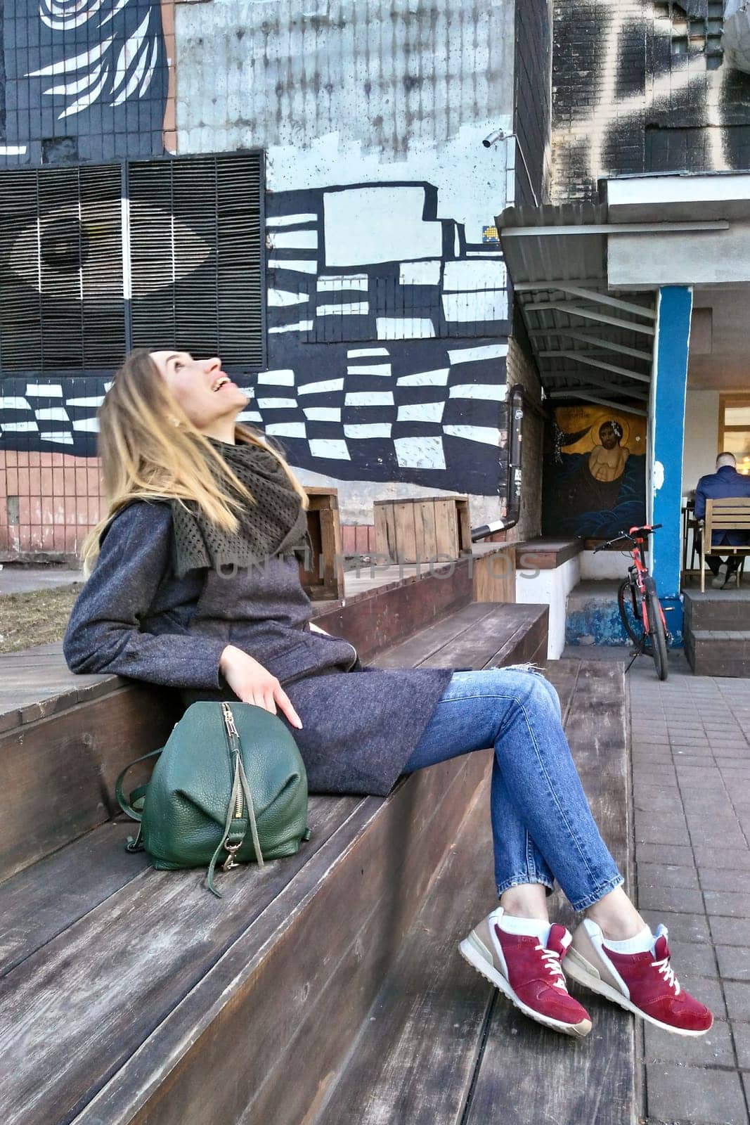 A young woman sits on a wooden staircase and laughs, lifting her head up