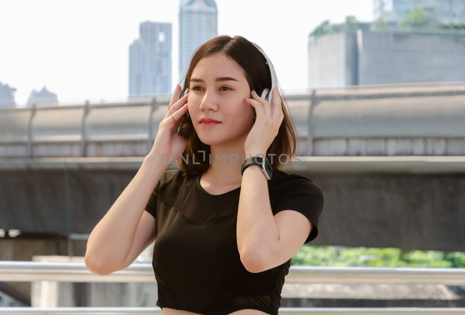 Young fitness woman listening to music on her headphones in urban background and relaxing after exercise. Healthy lifestyle concept.