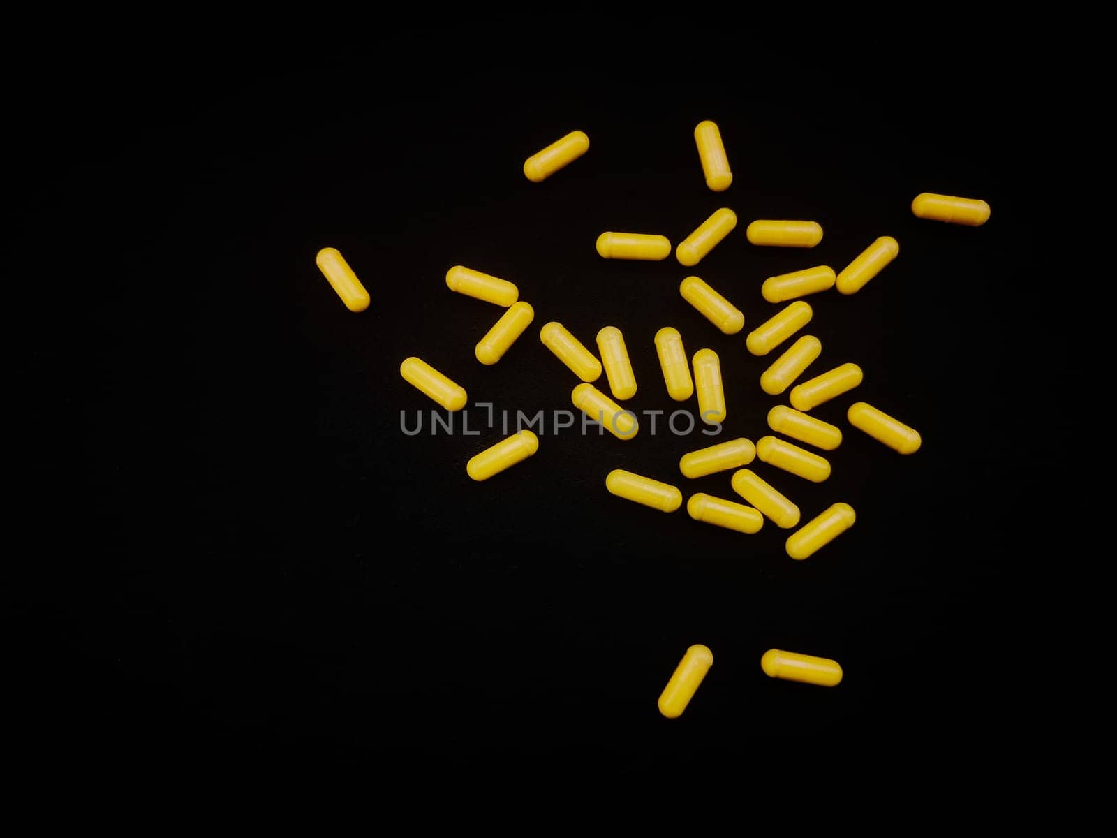 A handful of yellow capsules are scattered on a black background, copy space