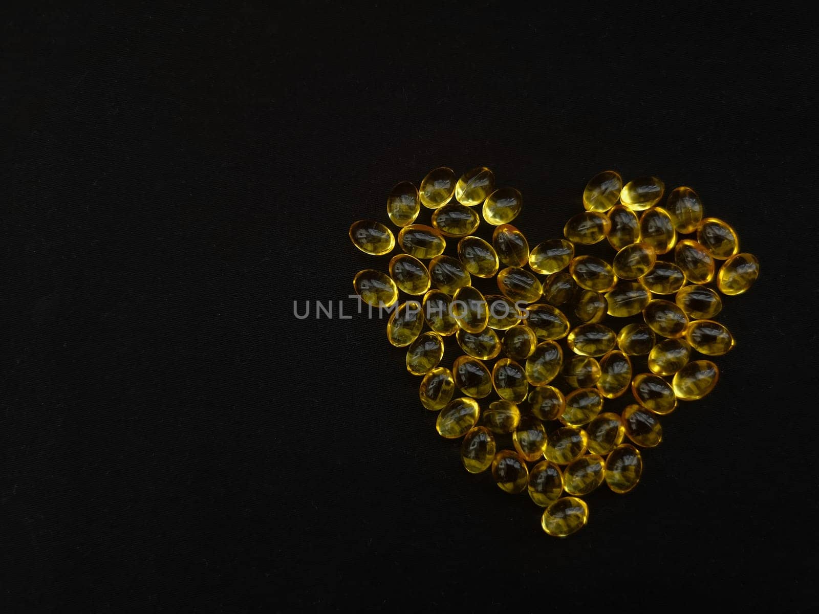 A handful of yellow transparent capsules on a black heart-shaped background, copy space for your text, view from above