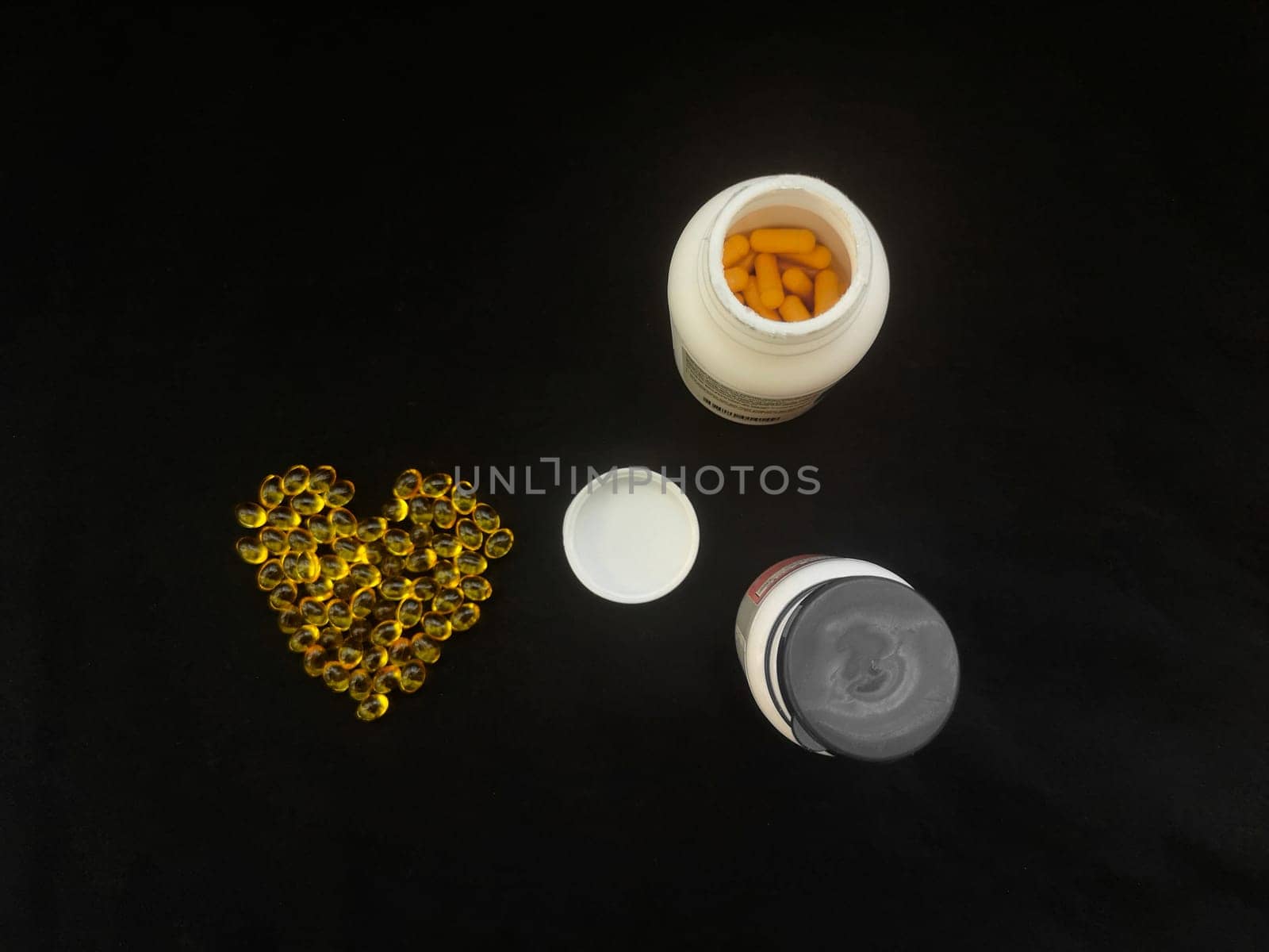 Yellow transparent heart-shaped capsules and jars of pills on a black background