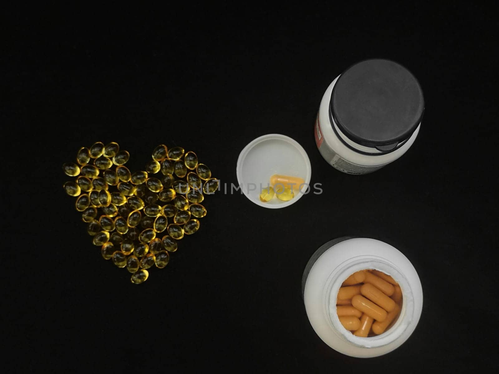 Two jars of medicine, a handful of yellow transparent heart-shaped capsules on a black background