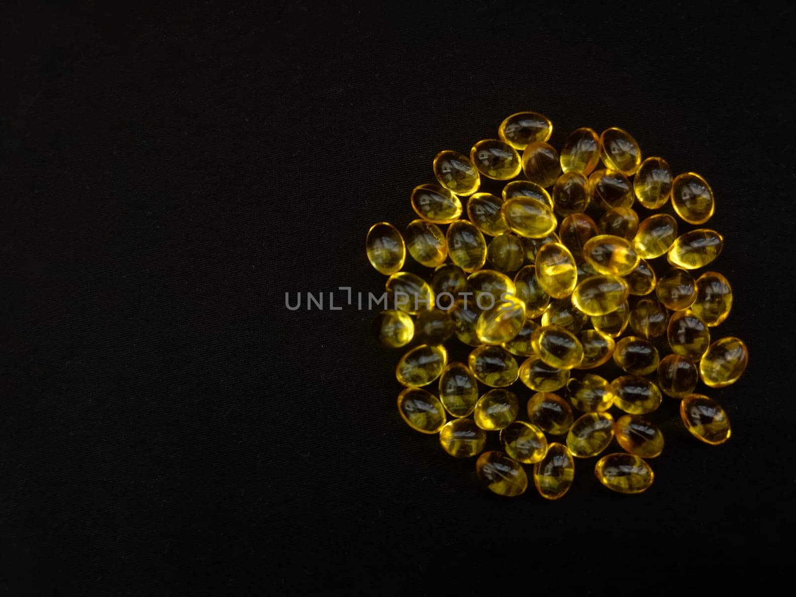 A handful of yellow transparent capsules on a black background in the shape of a circle, copy the space, view from above