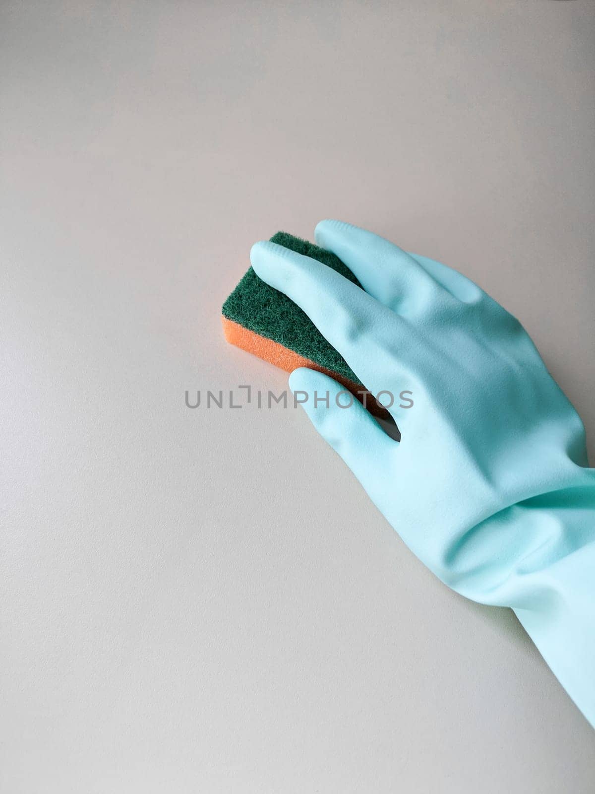 Cleaning and disinfection. A woman in a blue glove holds an orange sponge and washes a light wall.