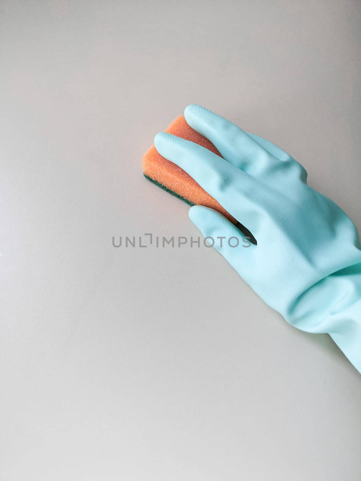 Cleaning and disinfection. A woman in a blue glove holds an orange sponge and washes a light wall.