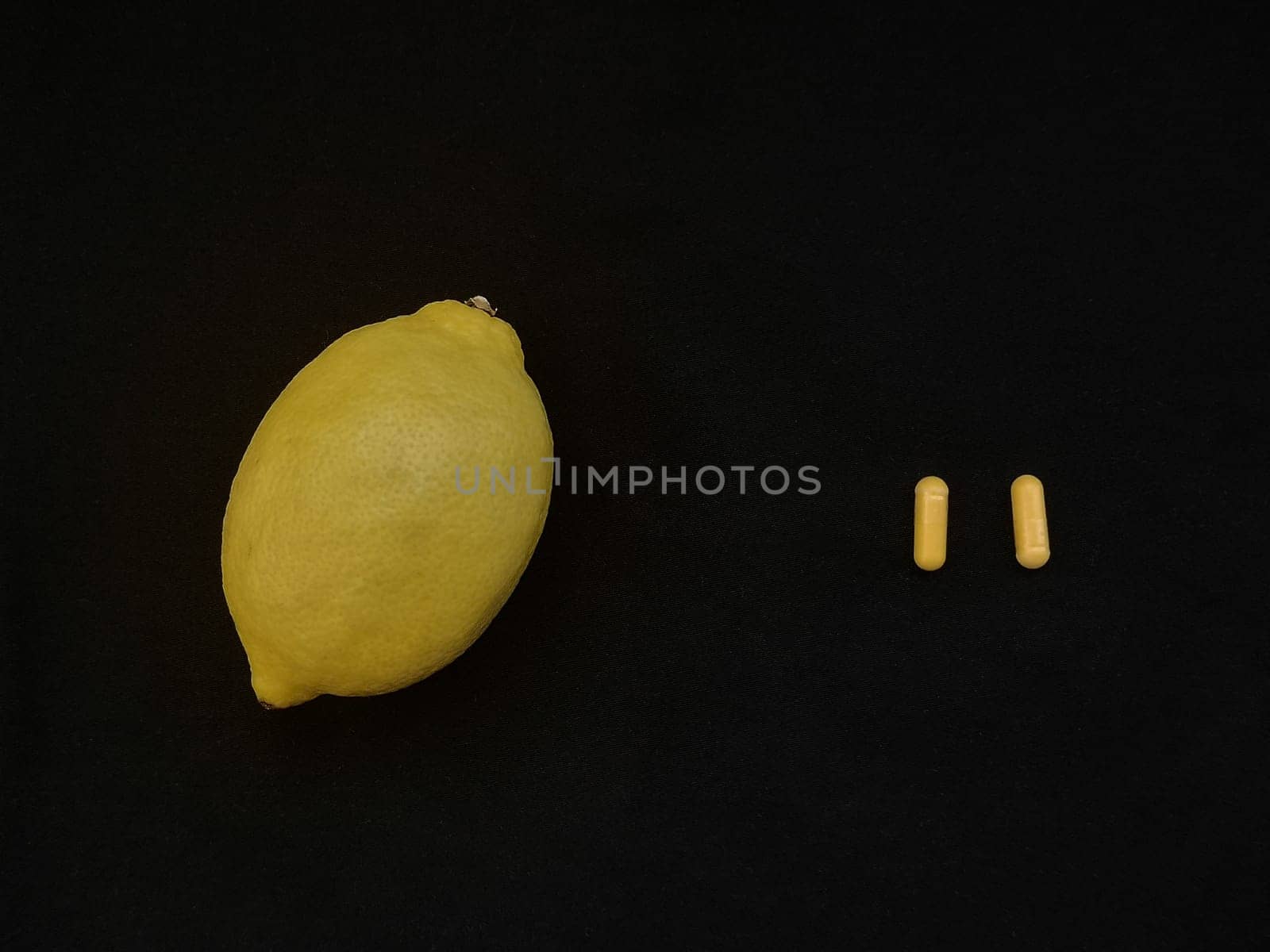 Two yellow capsules and lemon on a black background, View from above, copy space