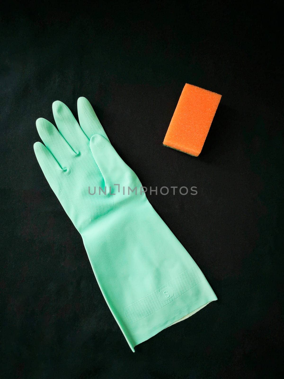 Cleaning and disinfection. A green rubber glove and an orange sponge on a black background. View from above. Flat lay.