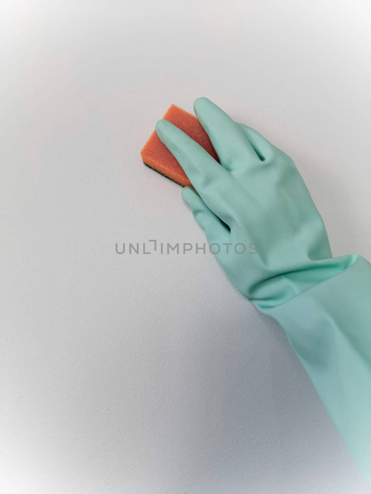 Cleaning and disinfection. A woman in a blue glove holds an orange sponge and washes a light wall.