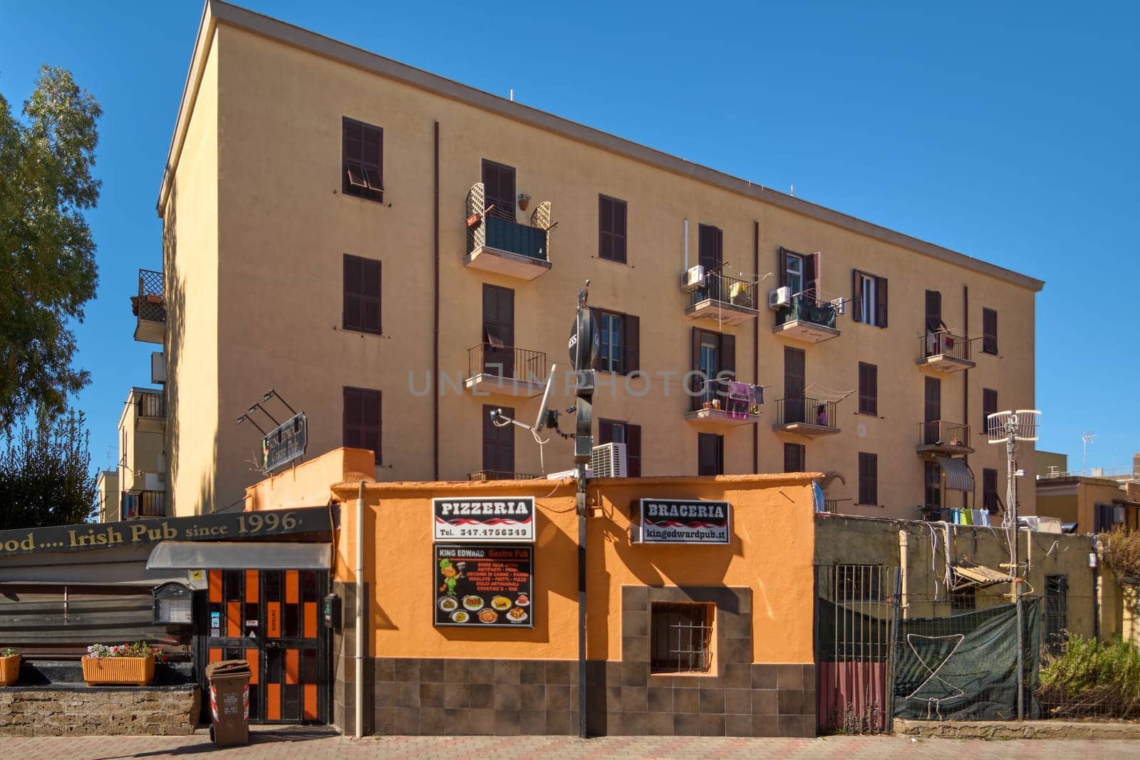 Civitavecchia. Italy - December 27, 2024: Italian street with residential buildings and local shops Signs of pizzeria and brazier on the ground floor and balconies Concept: community life and commerce