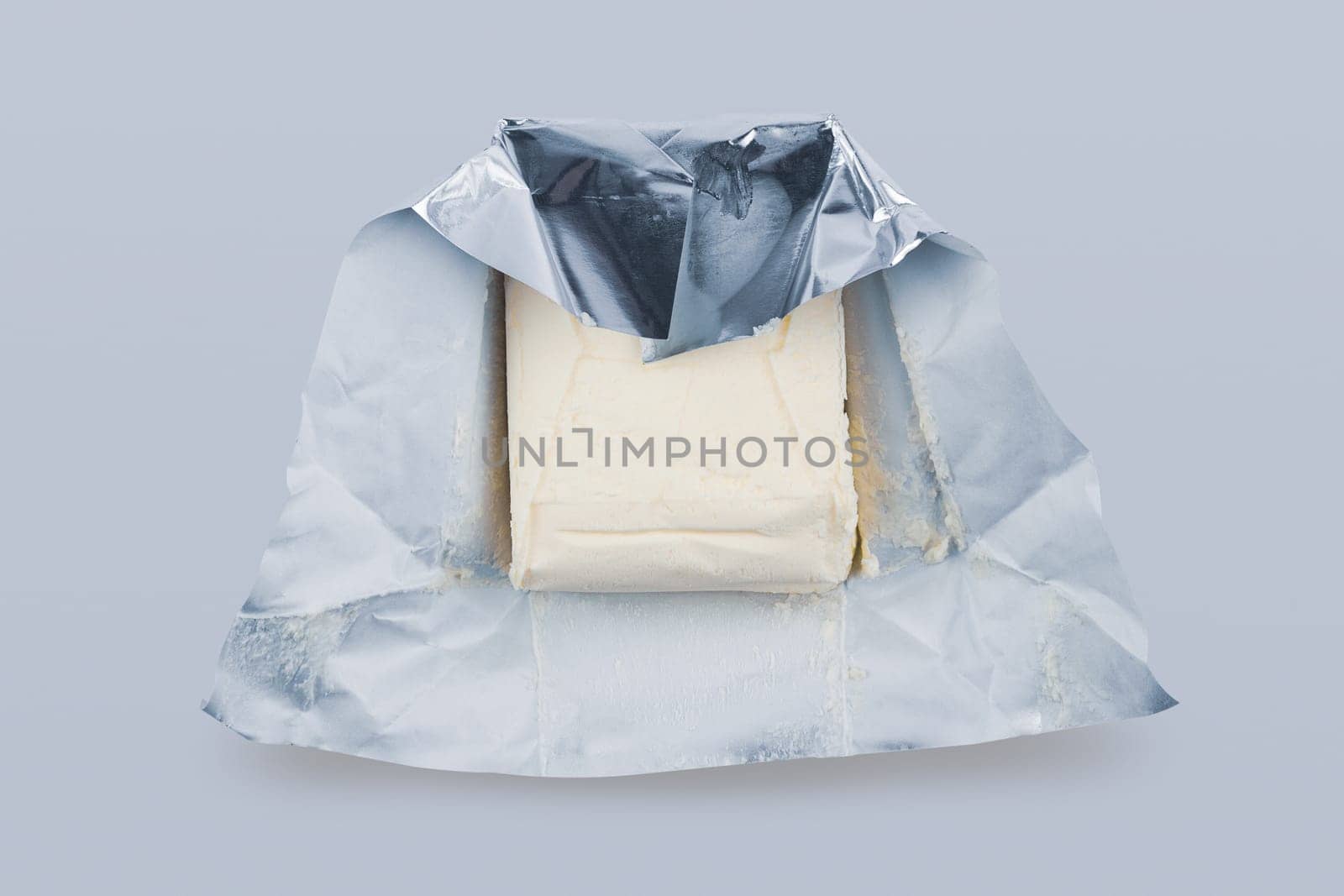 top view closeup of opened fresh piece of butter in silver foil protective packaging on grey background
