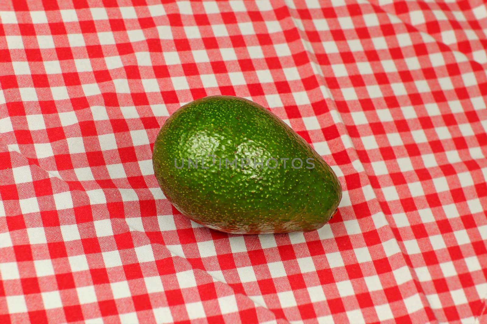 Whole avocado on red checkered tablecloth