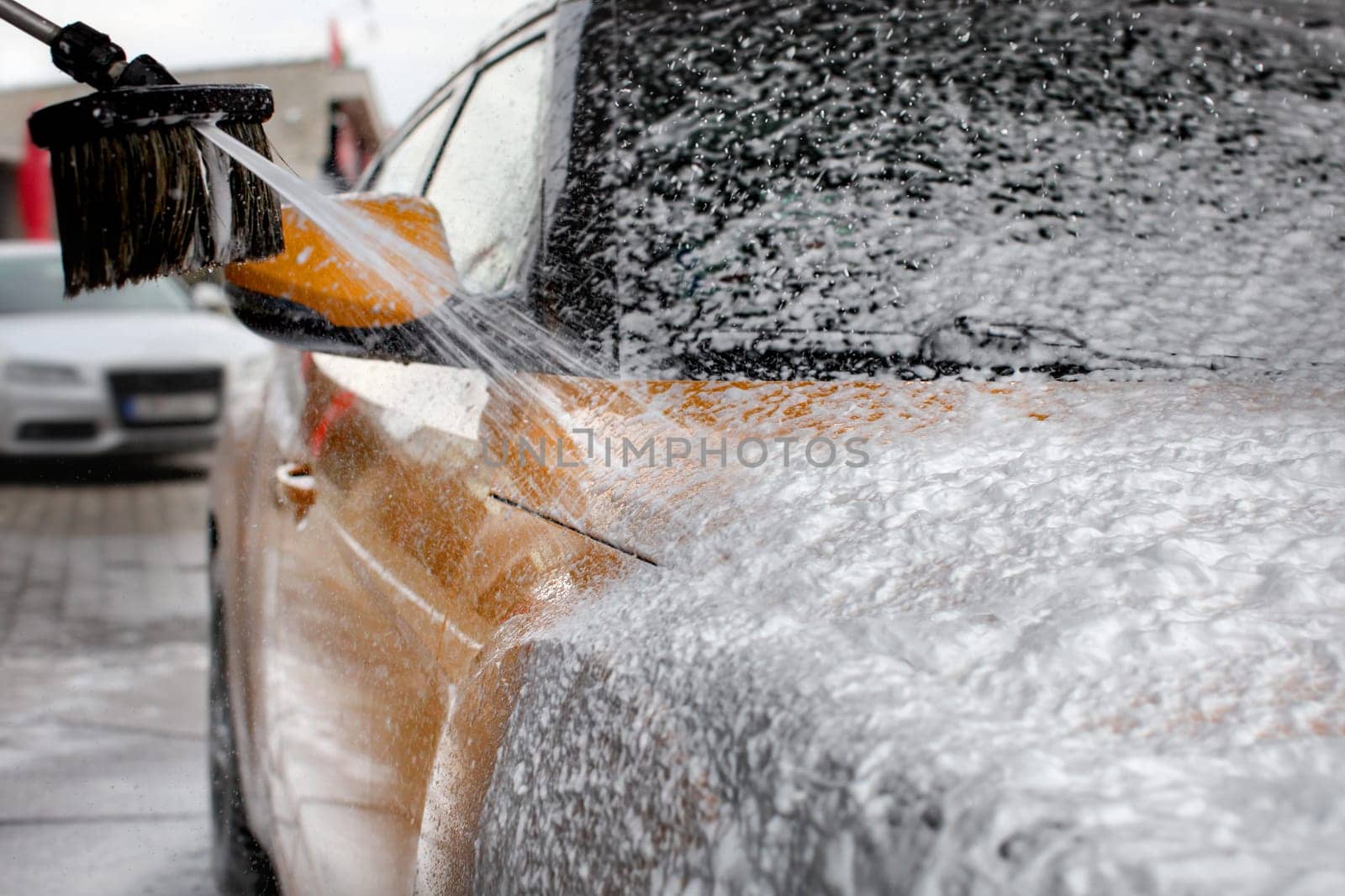 Water and shampoo stream falling on car covered with thick foam, when washed in carwash.