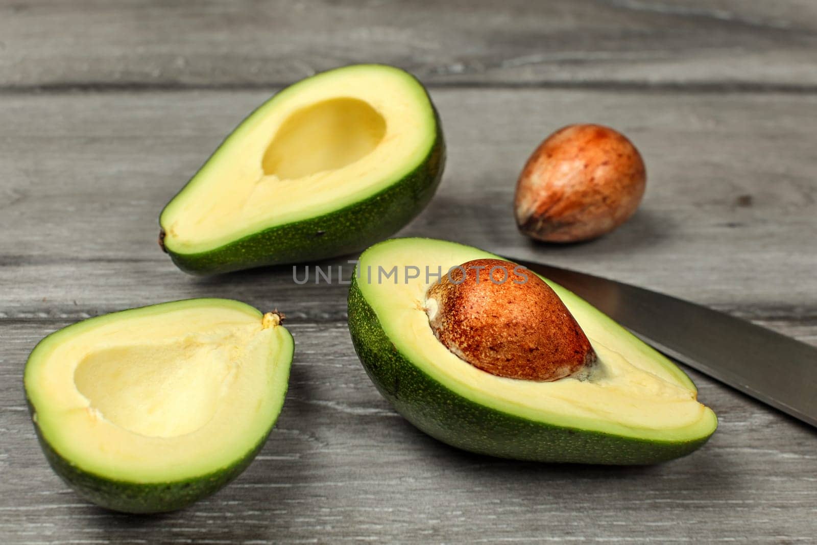Avocado, cut in half, two seeds and chefs knife on gray wood desk.