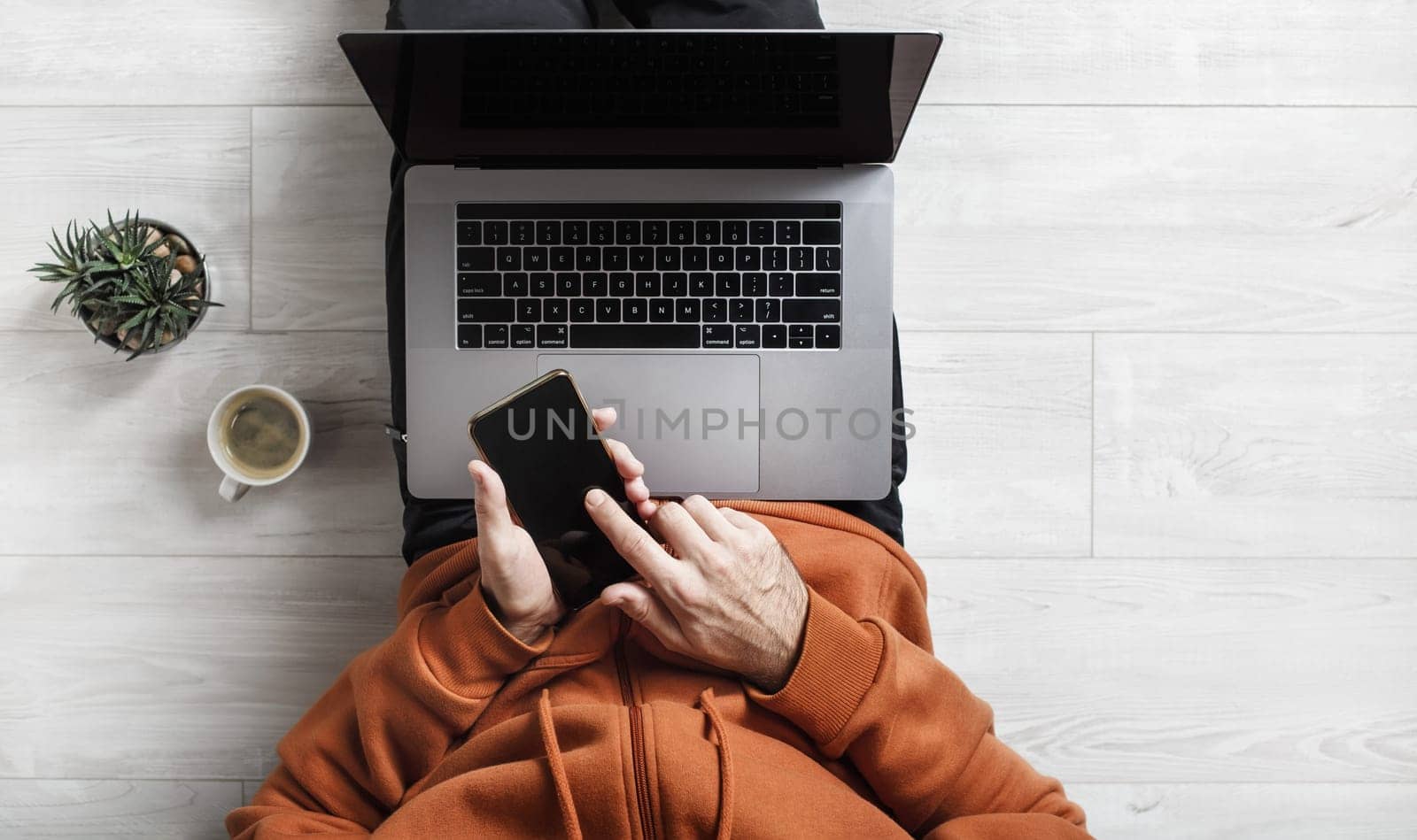 Work at home. Laptop and smartphone in the hands of a man. Businessman or freelancer at work sits on a wooden floor.