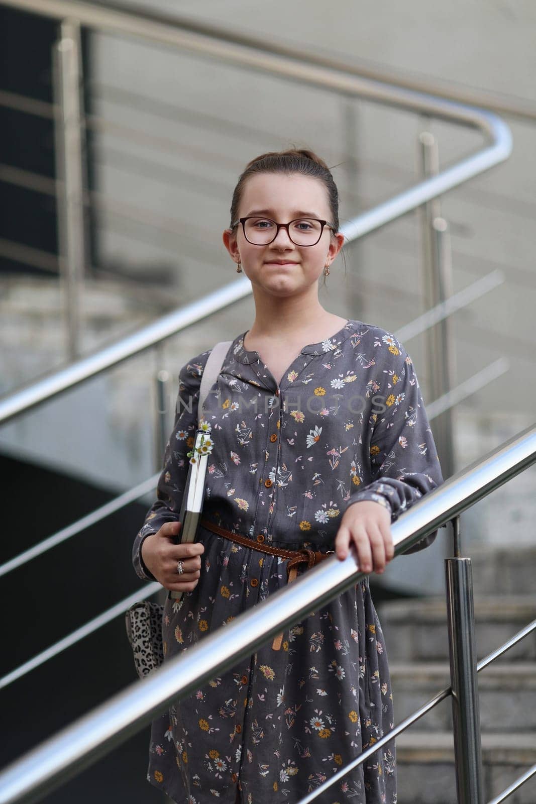 Girl posing while standing on the stairs with a book in her hands. Child on the background of the railing. Selective focus.