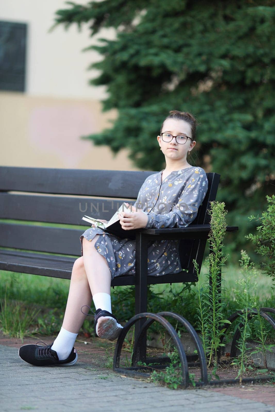 Pensive girl sits on a bench with book in her hands. Selective focus.