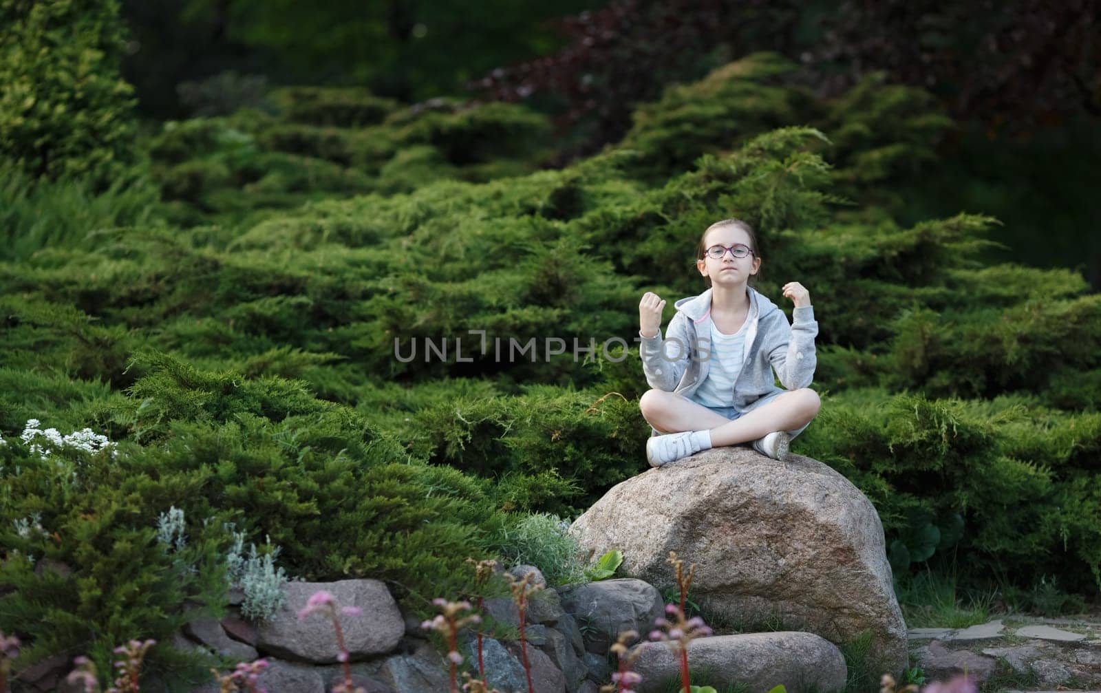 Child girl sitting on the cobblestone in lotus position. Teenage girl practicing yoga.