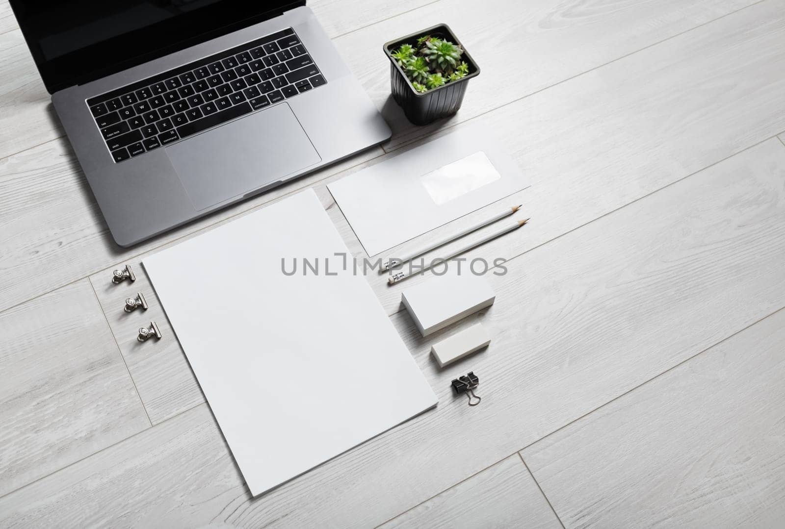 Photo of blank stationery set and laptop on wooden background.