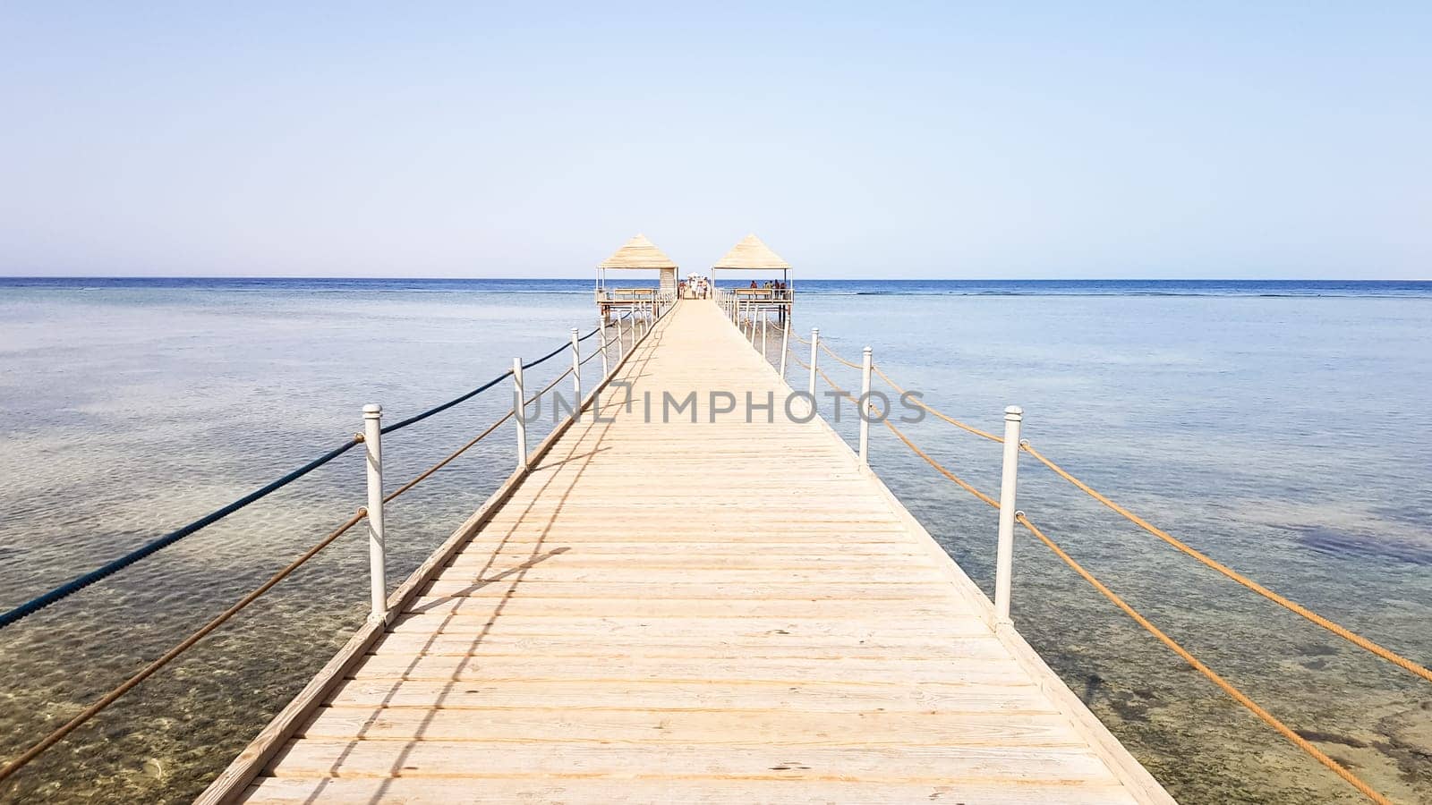 Long pontoon on the Red Sea in Egypt. Pontoon for descent into the water. Wooden bridge on the territory of the Amway Hotel in Sharm El Sheikh with metal fences and a rope over the sea with waves.