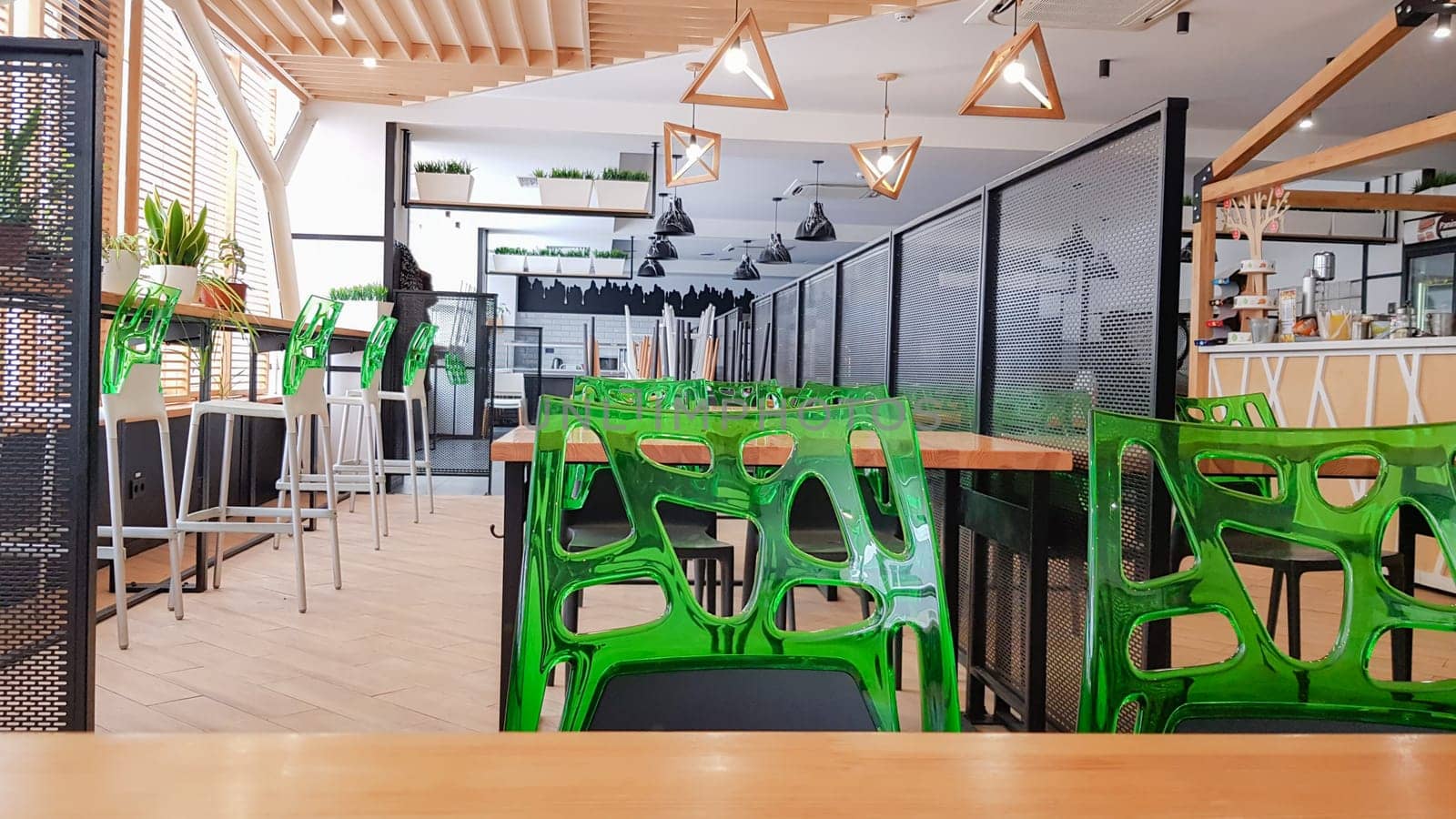 Cafeteria, no people dining room with wooden tables and green chairs. Interior with wood and metal elements. Modern dining areas with window lighting. Ukraine, Kiev - February 19, 2021.