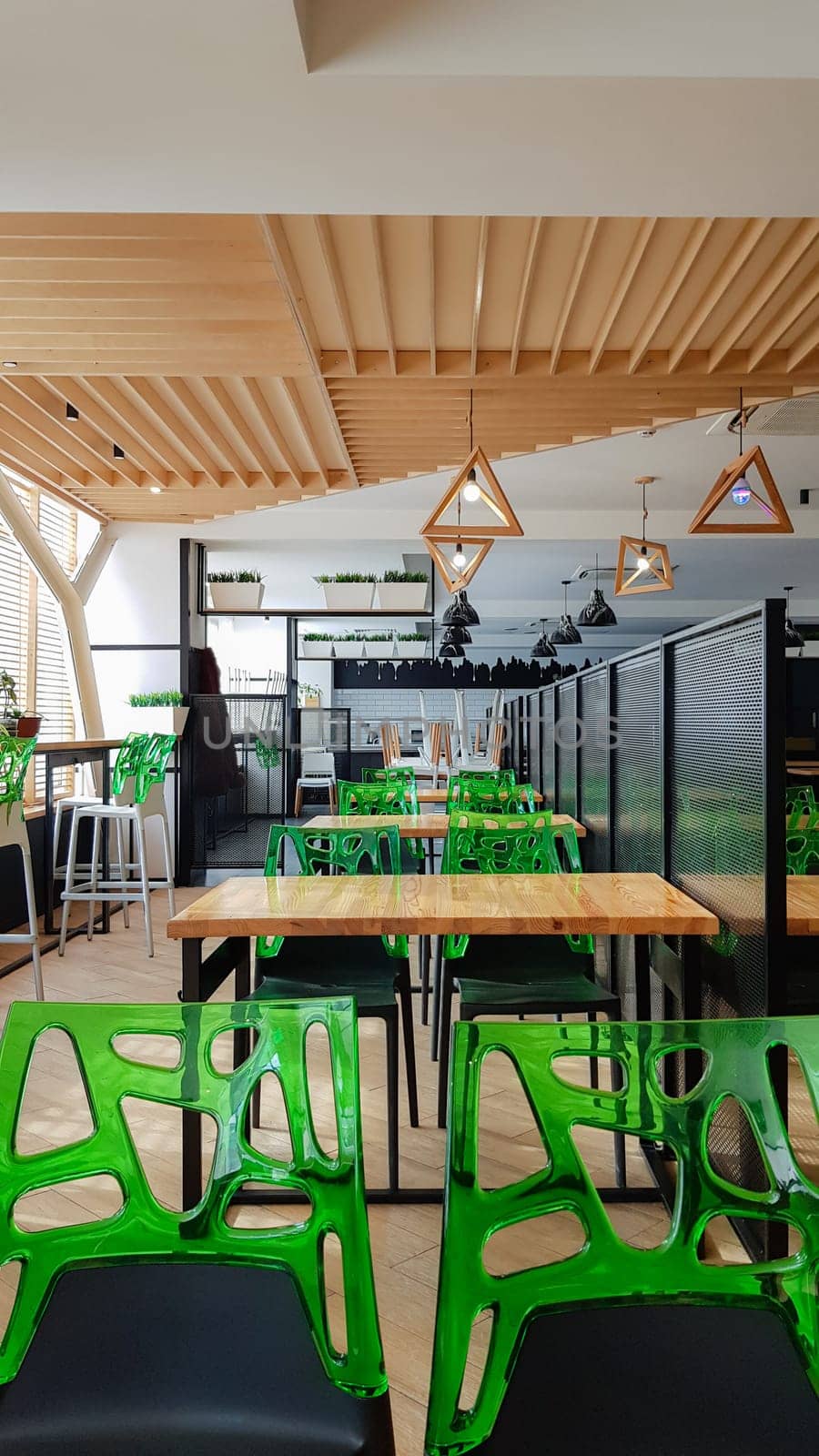 Cafeteria, no people dining room with wooden tables and green chairs. Interior with wood and metal elements. Modern dining areas with window lighting. Ukraine, Kiev - February 19, 2021.