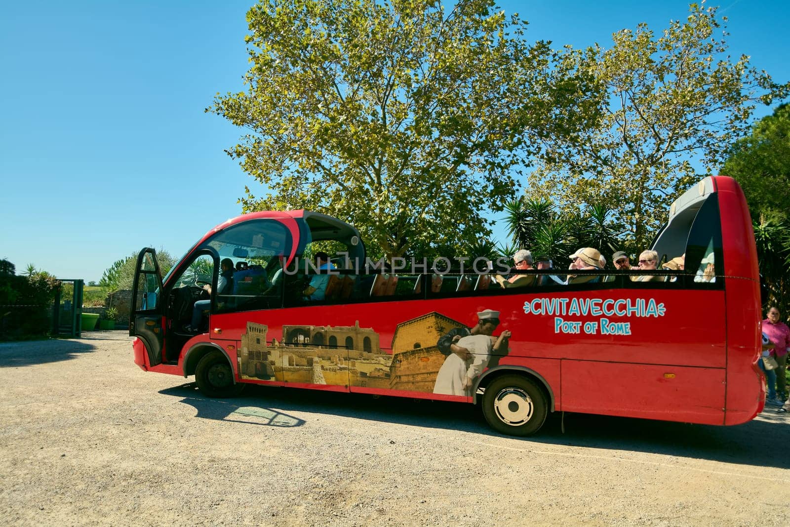 Civitavecchia. Italy - January 25, 2025: Tourists enjoying  sunny day on a red open top bus in Civitavecchia Italy The bus is adorned with local landmark images and the text Civitavecchia Port of Rome