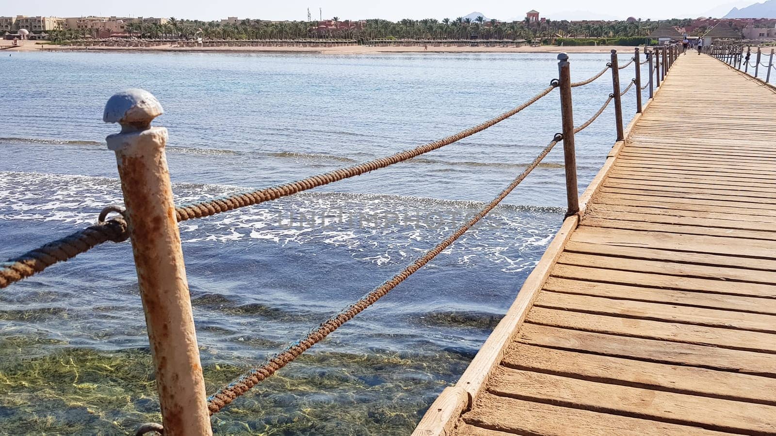 Long pontoon on the Red Sea in Egypt. Pontoon for descent into the water. Wooden bridge on the territory of the Amway Hotel in Sharm El Sheikh with metal fences and a rope over the sea with waves.
