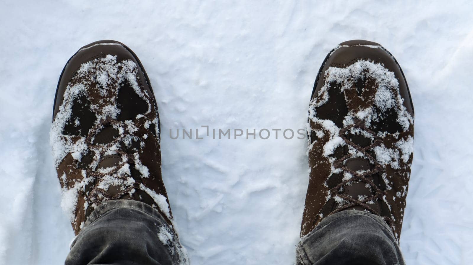 Male legs in snow-covered winter boots, top view. Winter walk in the snow. Focus on your legs. Beautiful white winter weather with fresh snowfall