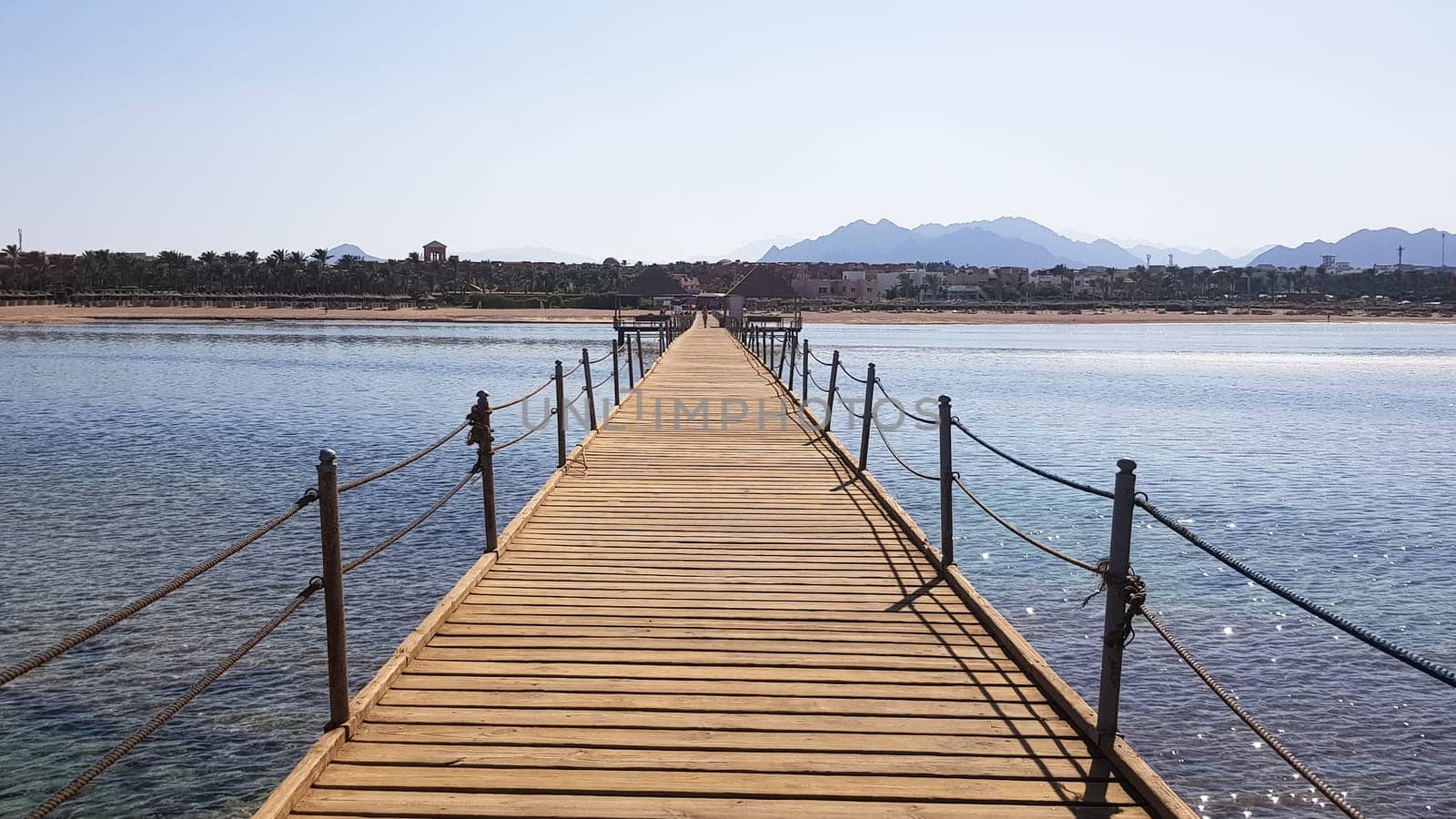 Long pontoon on the Red Sea in Egypt. Pontoon for descent into the water. Wooden bridge on the territory of the Amway Hotel in Sharm El Sheikh with metal fences and a rope over the sea with waves.