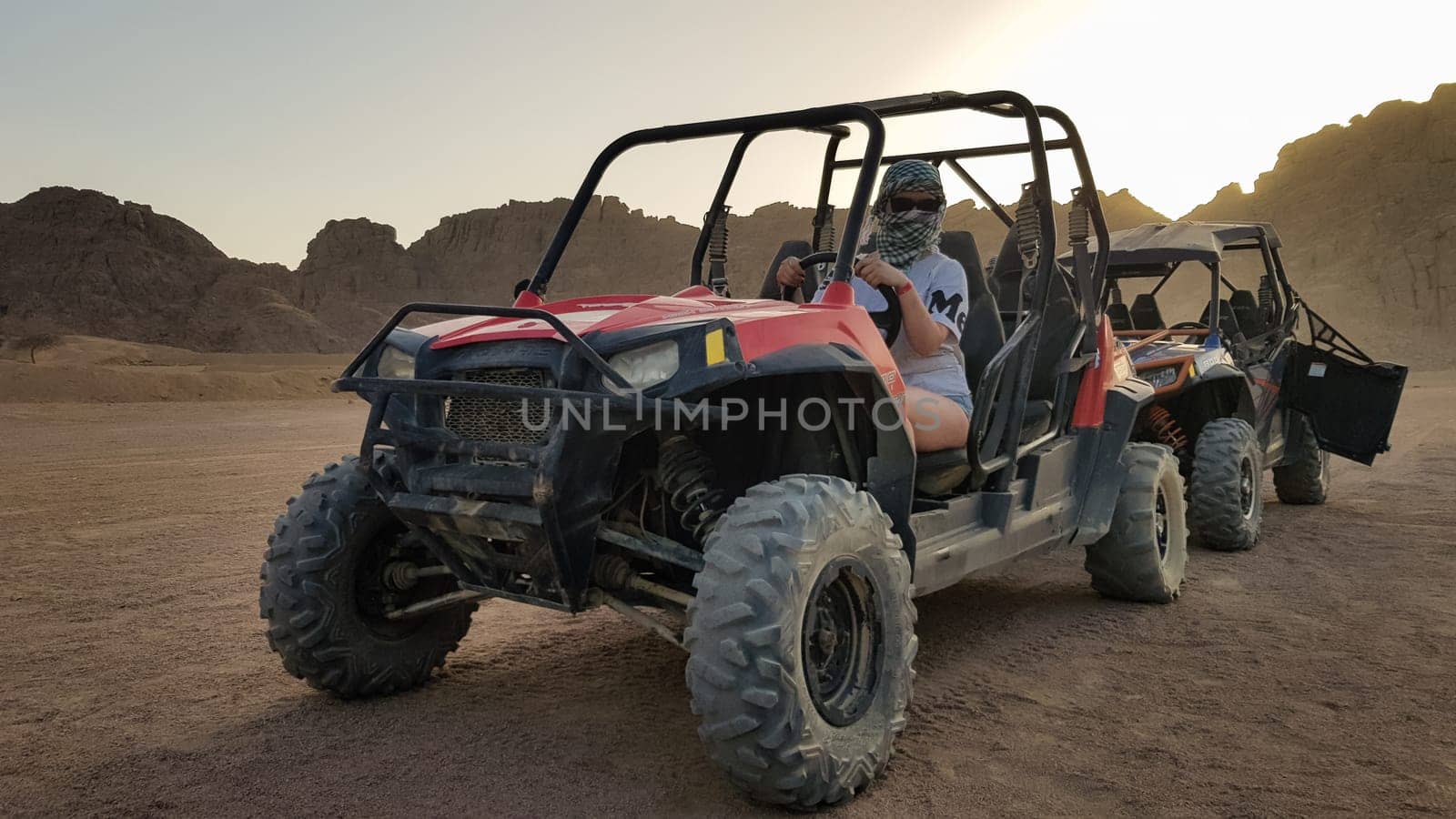 Egypt, Sharm El Sheikh - October 10, 2020. Active woman driving an ATV on a dirt road in the desert against the backdrop of rocky sandy mountains in the sunset