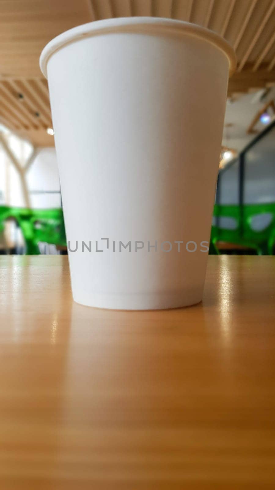 Paper white coffee cup disposable to take or go, on the wooden table of the coffee shop or dining room, place for a designer layout. Hot coffee cup in a cafe