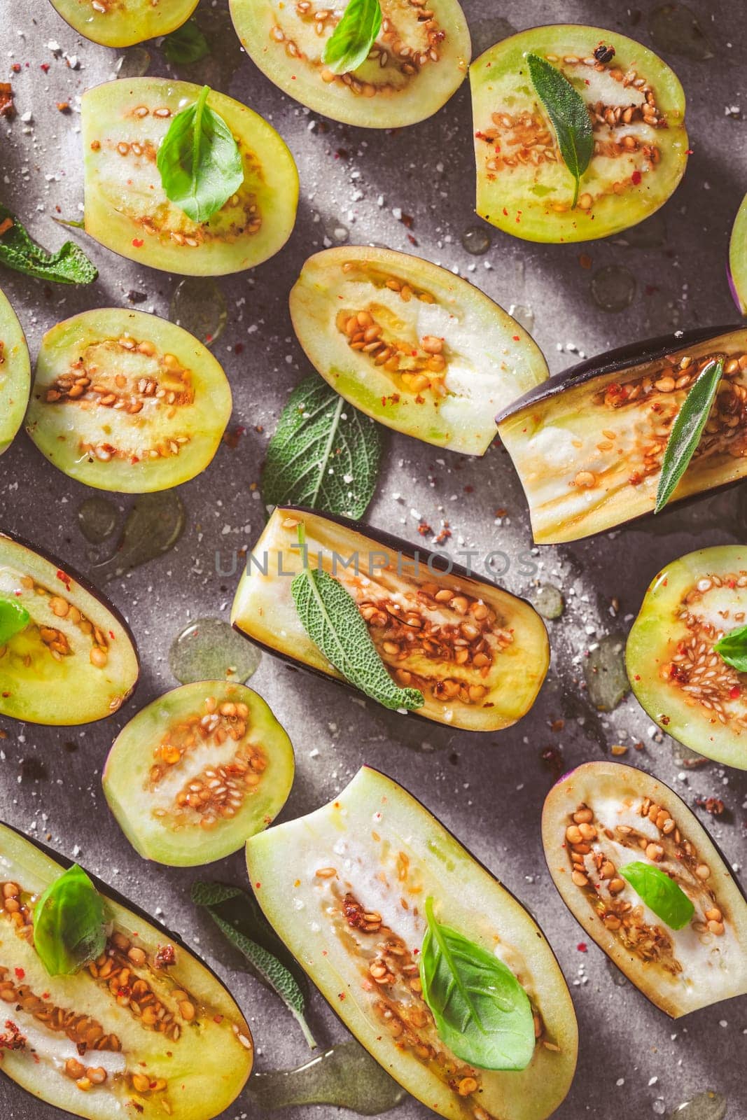 Small raw eggplants prepared for baking on baking sheet with herbs and spices