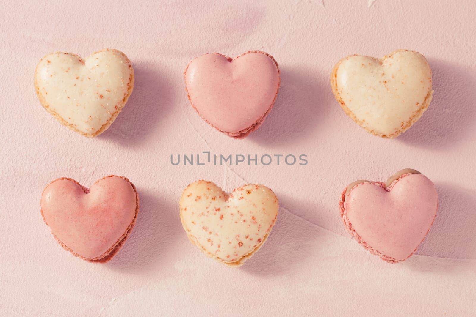 Delicious French macarons in heart shape on pink background