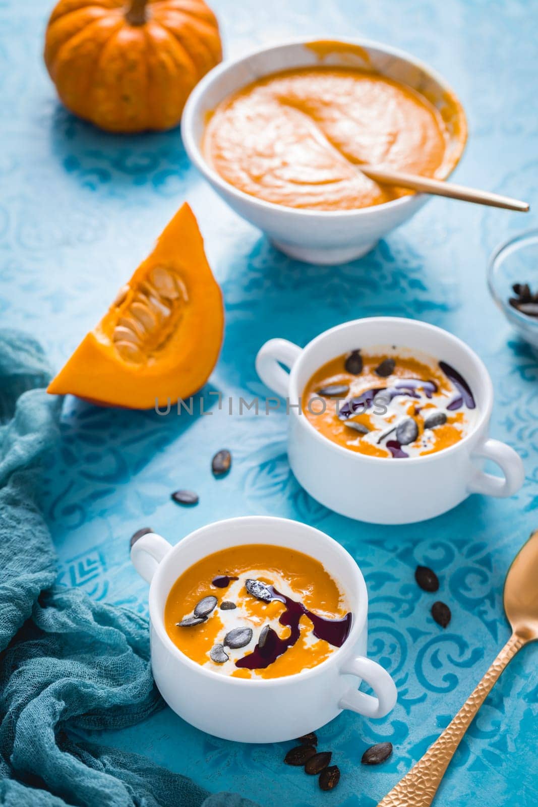 Homemade pumpkin soup with coconut milk, pumpkin oil and seeds on blue background