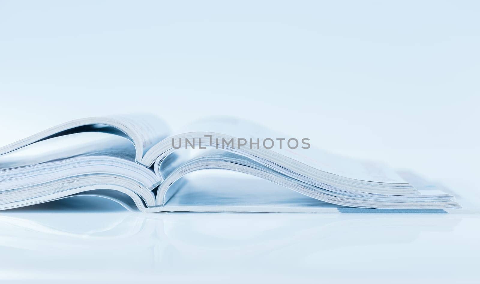 Stack of open magazines in blue tone on white background with copy space