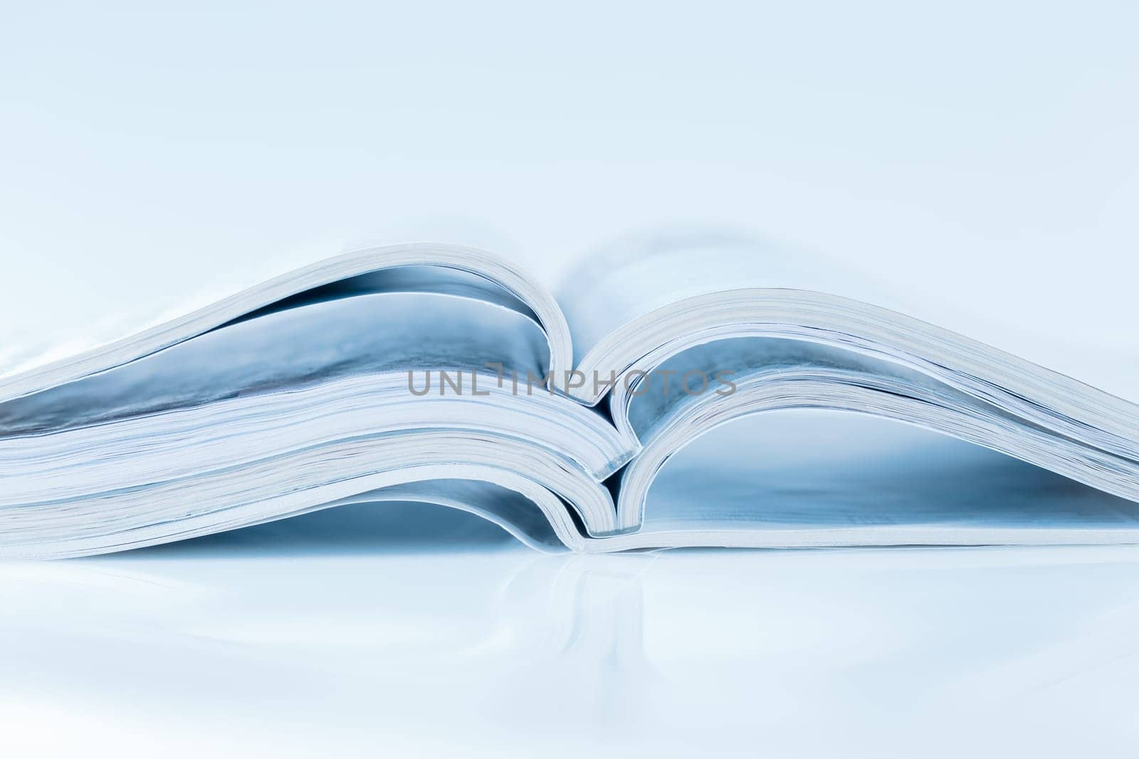 Stack of open magazines in blue tone on white background with copy space