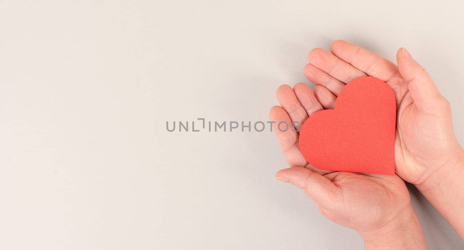 Woman is holding a red heart in her hand, world heart day, grey colored background, heartbeat, health issues