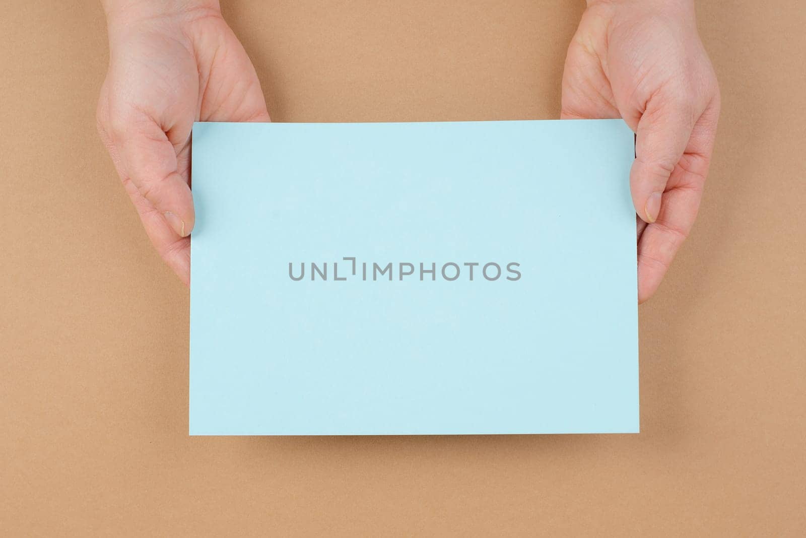 Woman holds a blank sheet of paper, brown colored background, empty copy space for text, minimalism