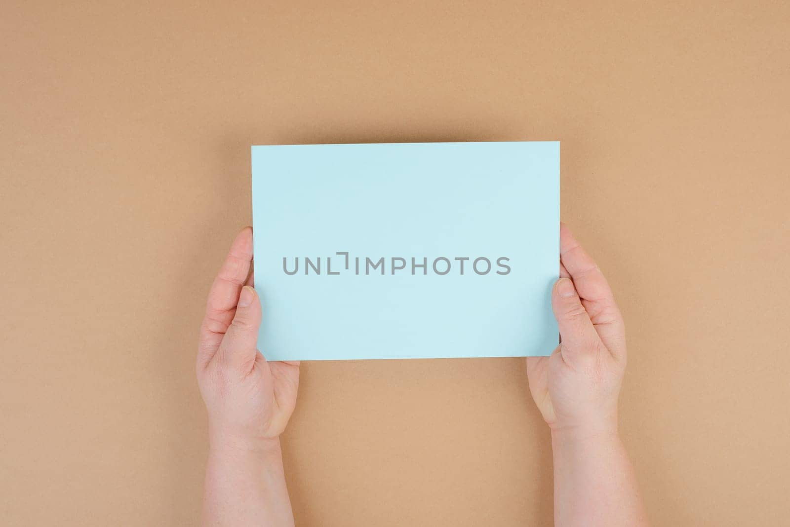 Woman holds a blank sheet of paper, brown colored background, empty copy space for text, minimalism