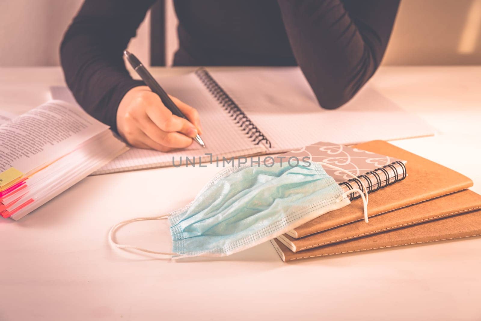 Detail of hands writing with school supplies and protective mask