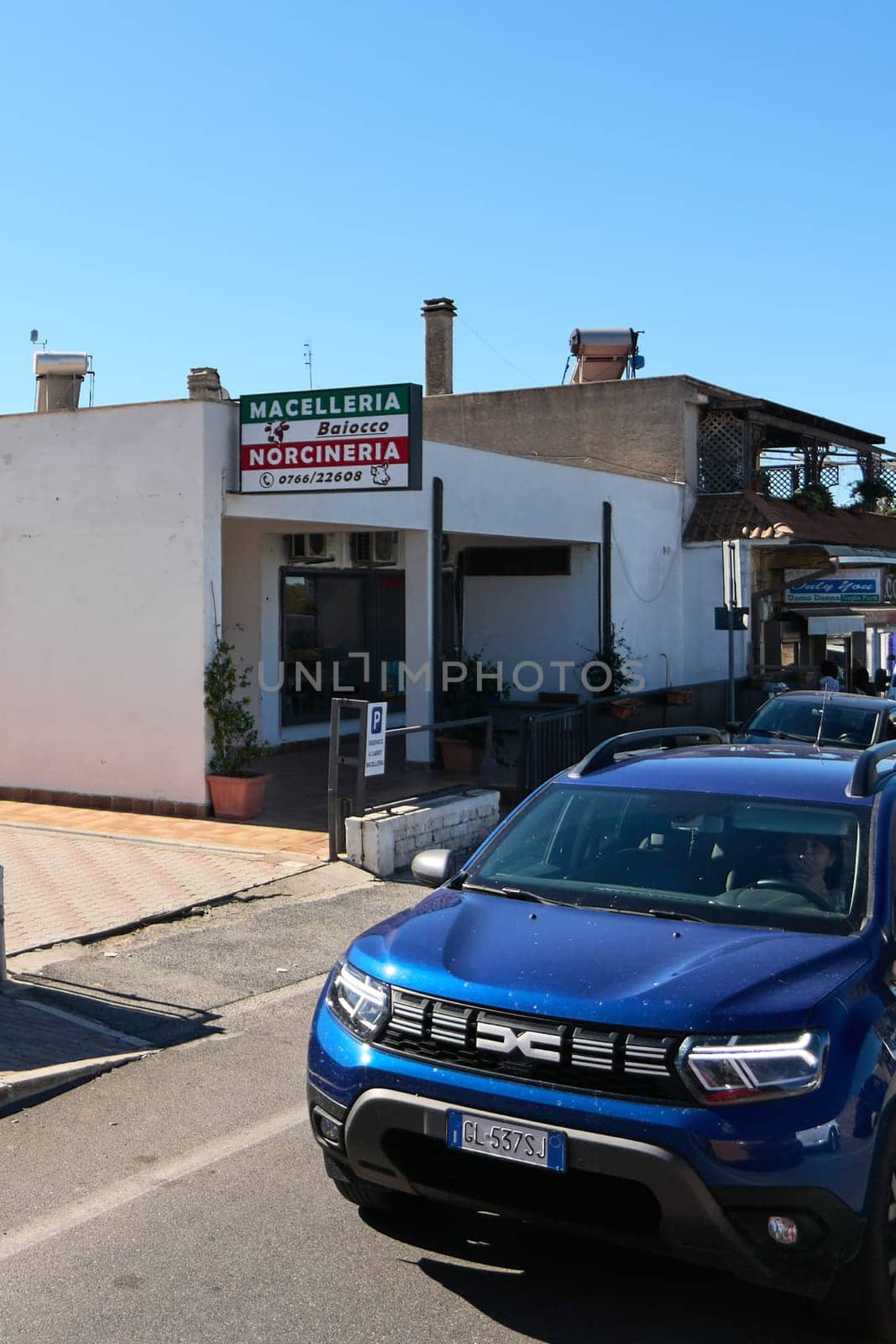 Civitavecchia, Italy - January 26, 2025: Italian butcher shop in Civitavecchia, with a sign with Macelleria Baiocco Norcineria and parked vehicles. A pedestrian stands near a black car
