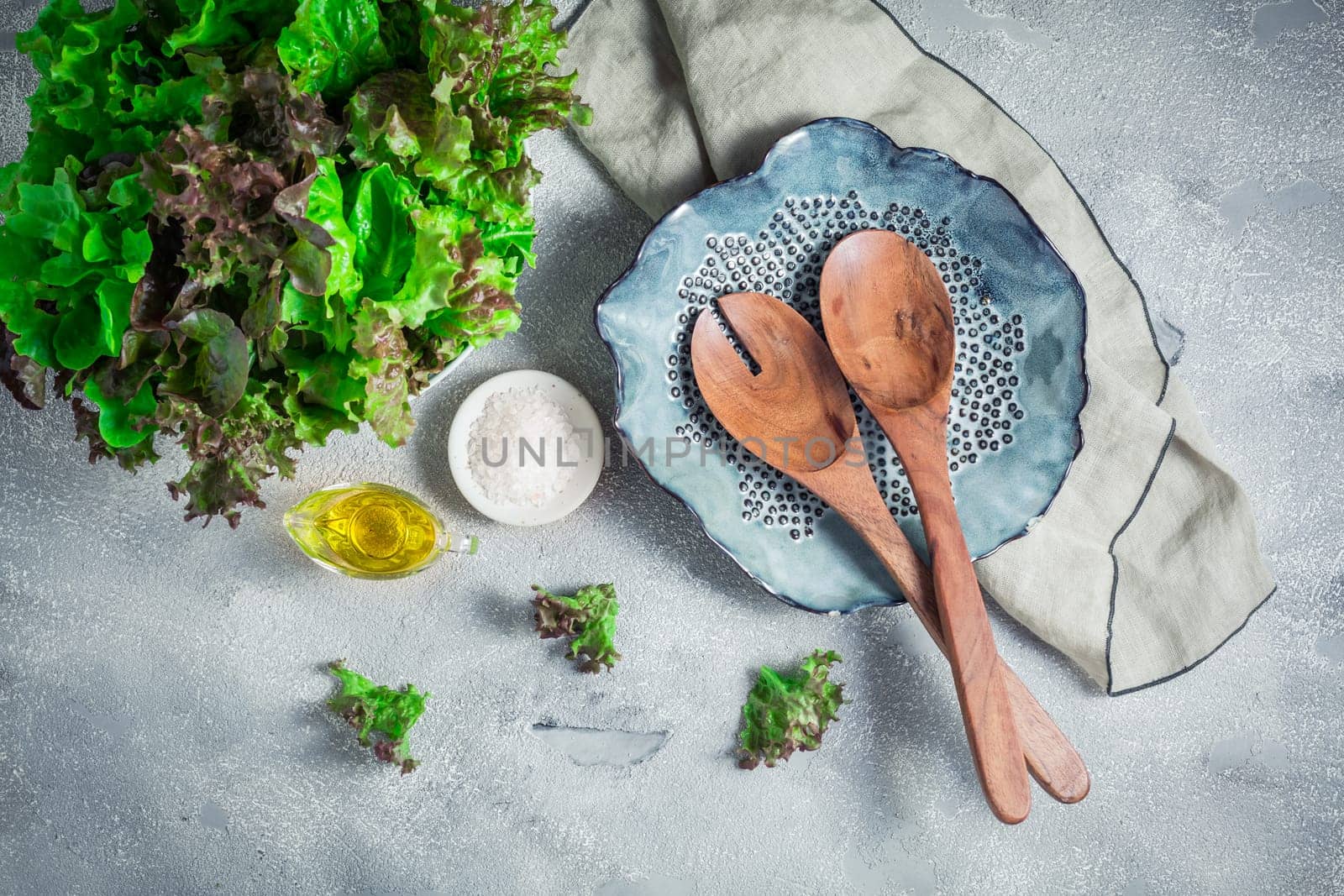 Modern ceramic bowl with wooden salad cutlery and bowl of lettuce on stone background