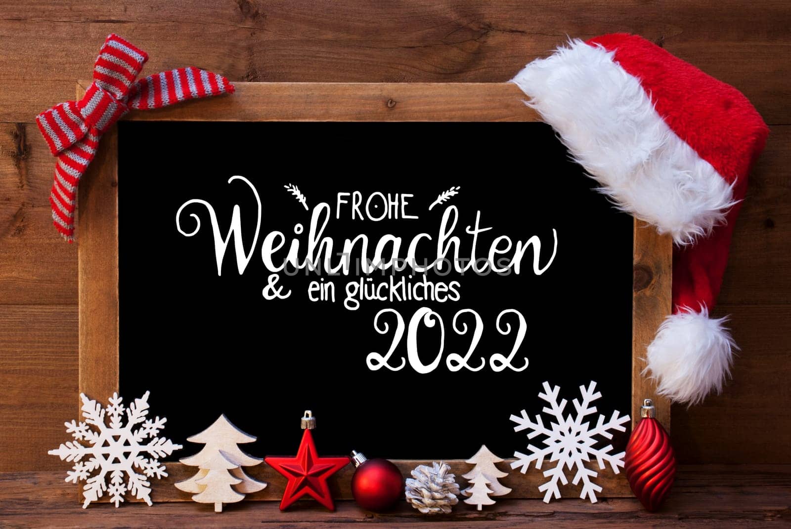 Chalkboard With German Calligraphy Frohe Weihnachten Und Ein Glueckliches 2022 Means Merry Christmas And A Happy 2022. Christmas Decoration Like Tree, Ball, Snowflake And Santa Hat. Wooden Background