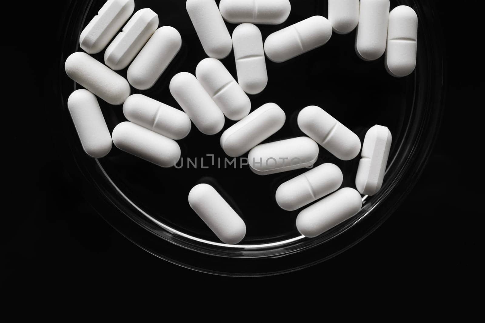 White medicine pills spilled on black background. Flat lay.