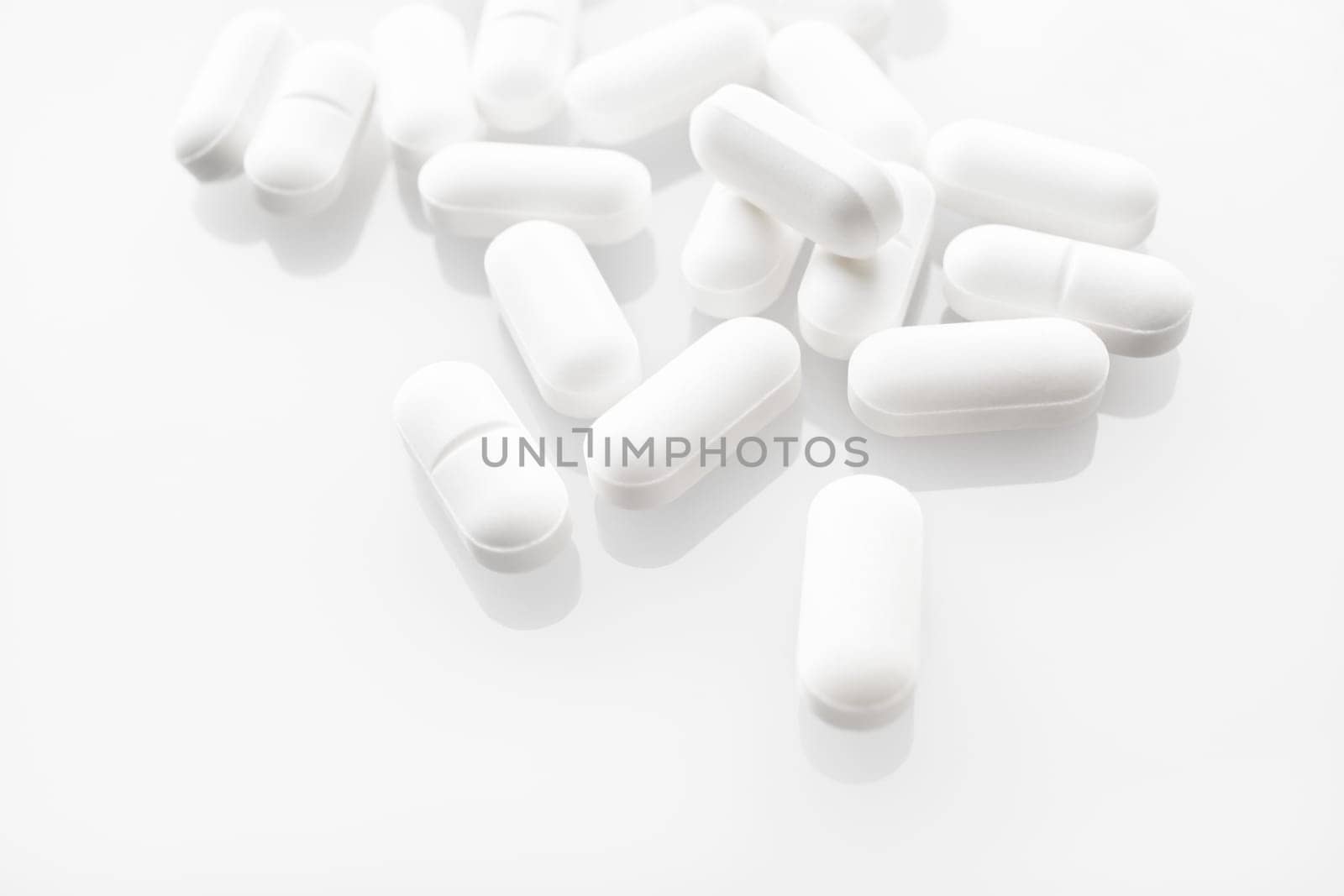 White medicine pills spilled on white background. Selective focus.