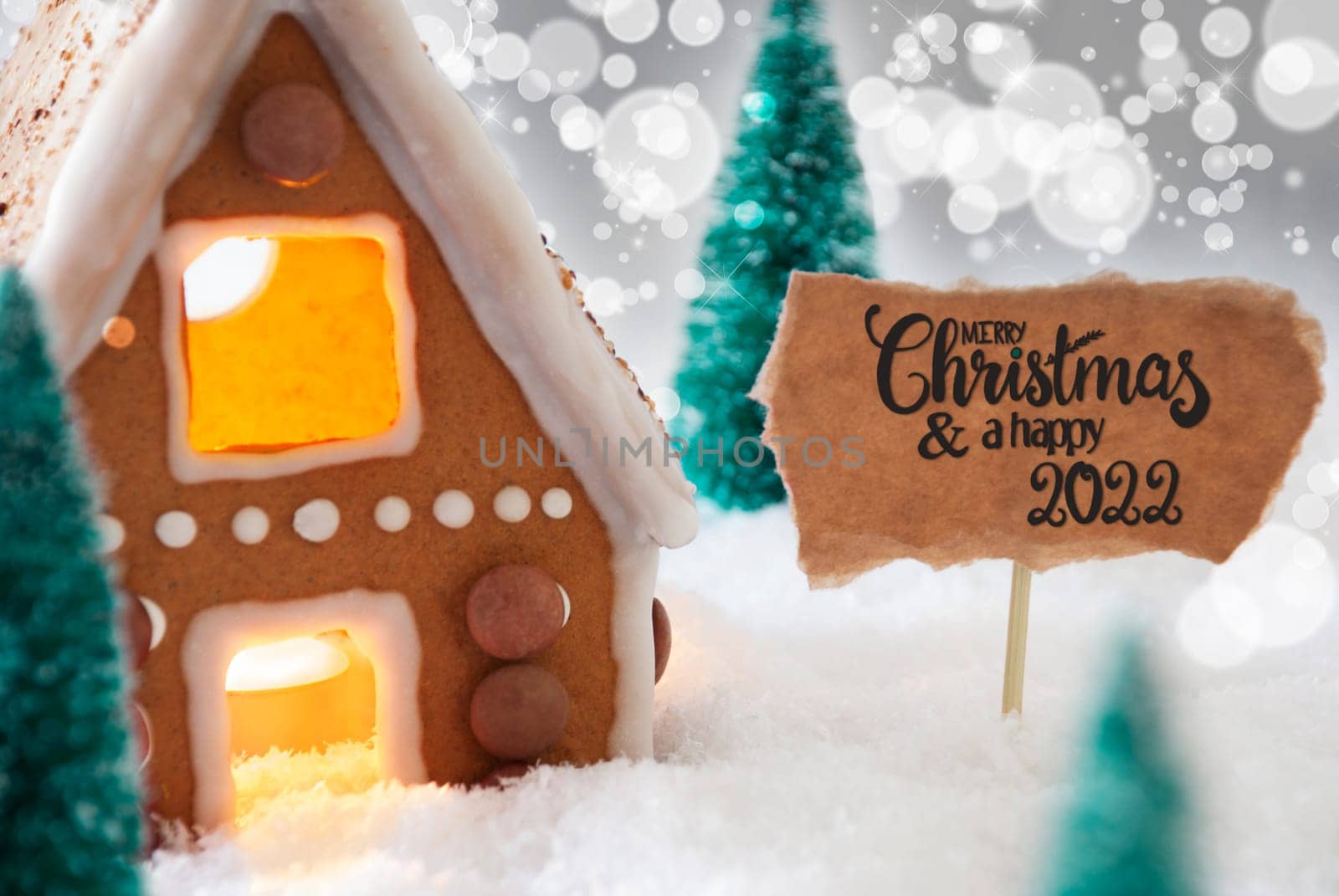 Sign With English Calligraphy Merry Christmas And A Happy 2022. Gingerbread House With Christmas Tree And Snow And Silver Sparkling Background