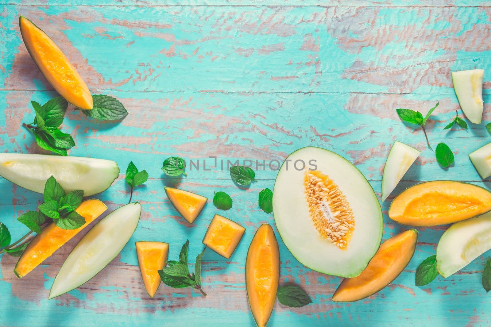 Healthy snack - Piel de sapo melon and cantaloupe with fresh mint on cyan wooden table