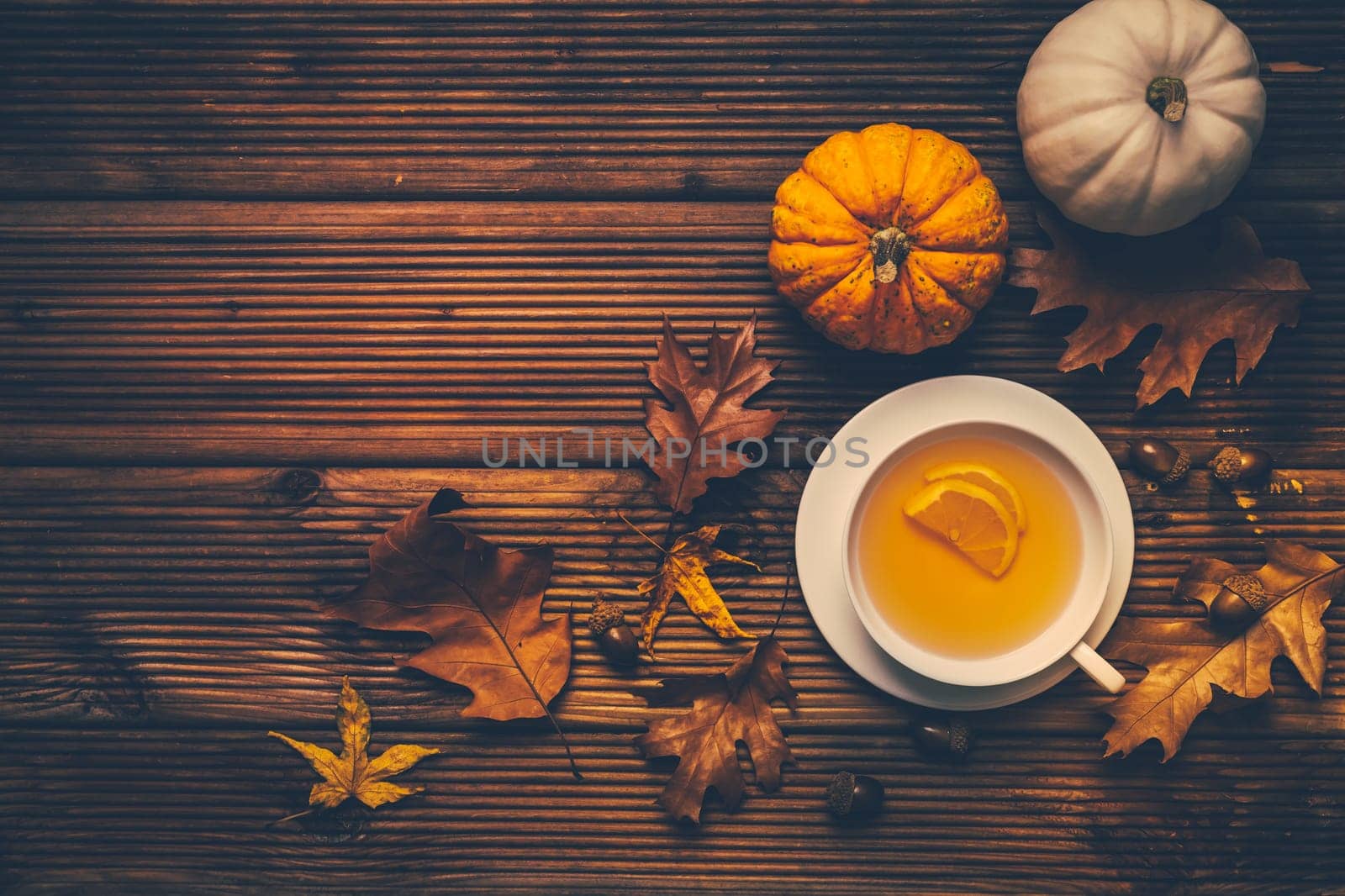 Hot lemon tea with fall foliage and pumpkins on wooden background